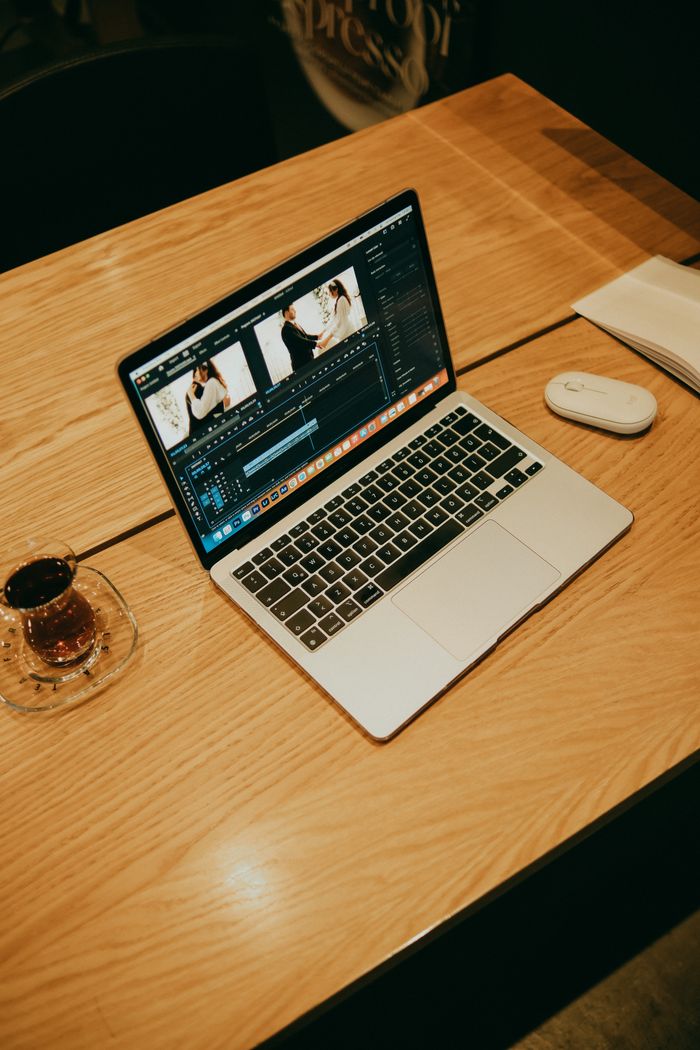 who-we-are A laptop on a wooden table in a coffee shop, displaying video editing software for creative work.